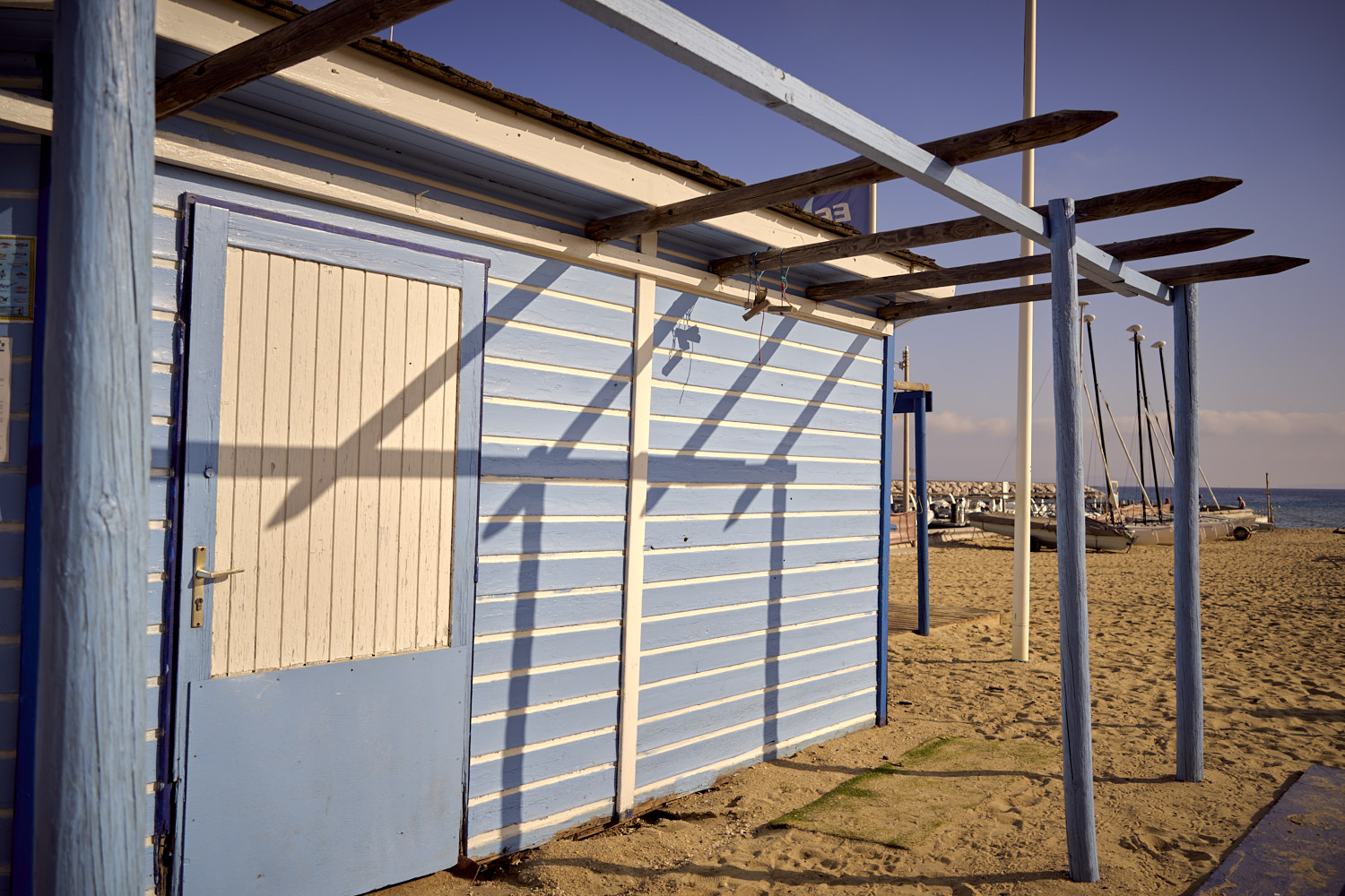 Strandh&uuml;tte mit Pergola-Dach am Strand, Boote und Meer im Hintergrund, Tageslicht